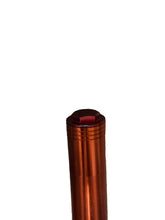 Load image into Gallery viewer, A close-up of a metallic copper-orange cylindrical object with a red top cap, resting on a brown wood floor.