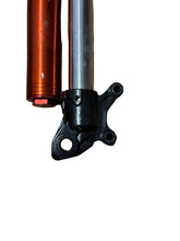 Load image into Gallery viewer, A close-up of a motorcycle front fork showing the black lower control arm and upper shock absorber, placed on a wooden surface next to an orange and silver fork section.
