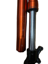 Load image into Gallery viewer, An orange anodized aluminum fork tube next to a silver metal fork leg and black shock absorber mount, placed on a wooden floor.

